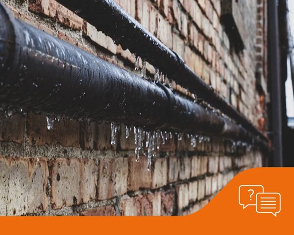 Frozen condensate pipes with icicles running along a brick wall outside a building