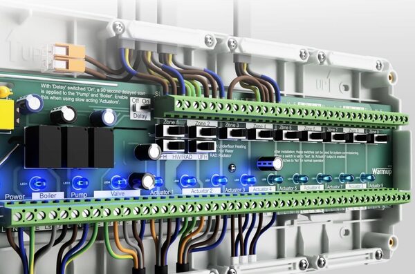 A Warmup underfloor heating wiring centre with green terminal blocks, labelled zones and actuators, and coloured wiring inside its enclosure