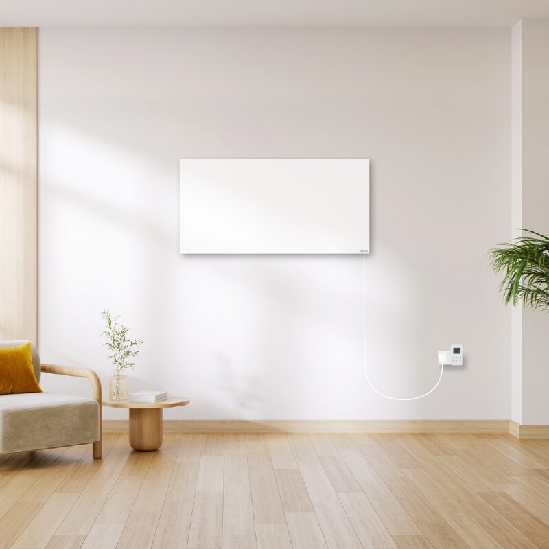 A white Herschel infrared heating panel mounted on a living room wall, plugged into a socket with a controller