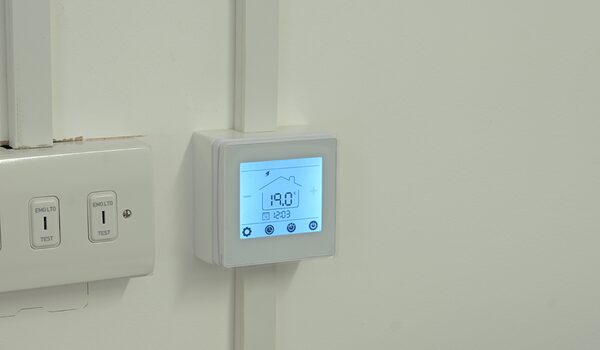 A white Herschel MD2 wired thermostat mounted on a wall next to an EMLOG test switch panel, displaying 19.0°C