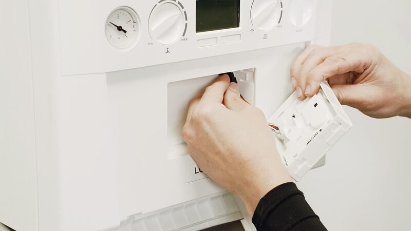 Hands plugging a white connector unit into the front of a white Ideal combi boiler