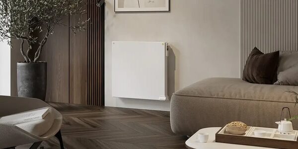 A white wall-mounted electric radiator installed in a modern living room beside a sofa