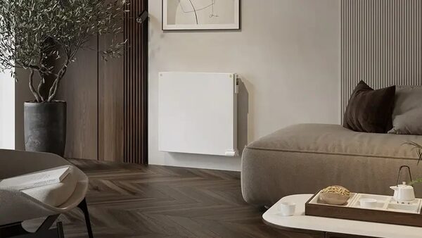 A white wall-mounted electric radiator installed in a modern living room beside a sofa