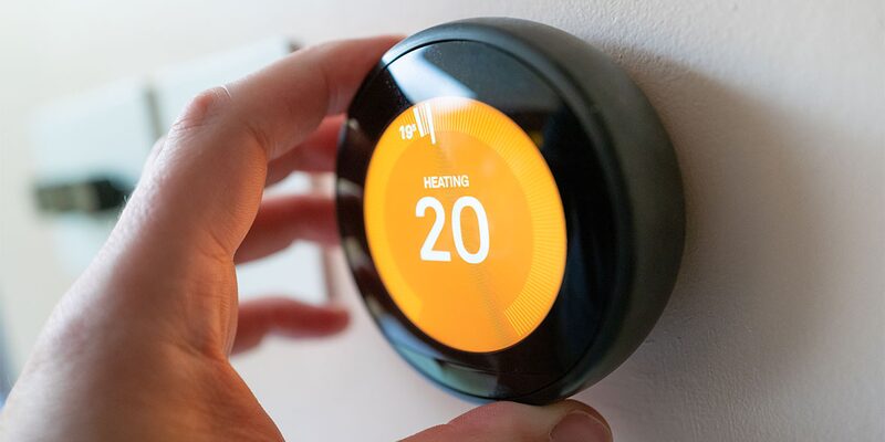 A hand adjusting a Google Nest smart thermostat on a wall, displaying heating set to 20 degrees