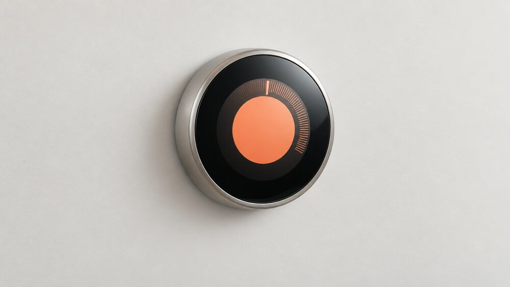 A round Google Nest Learning Thermostat mounted on a plain interior wall, shown close up with its circular dial face and metal ring, with nothing else in the frame.