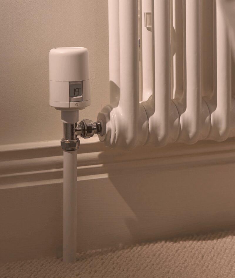 A white Hive smart thermostatic radiator valve fitted to a column radiator in a home, displaying 19 degrees