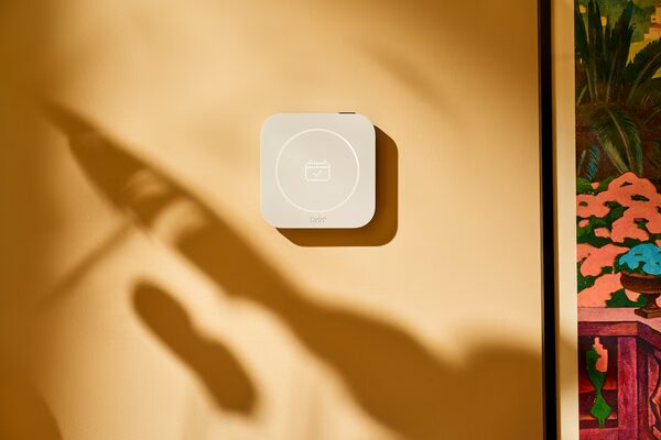 A white tado smart thermostat mounted on a warm yellow wall next to a colourful framed picture