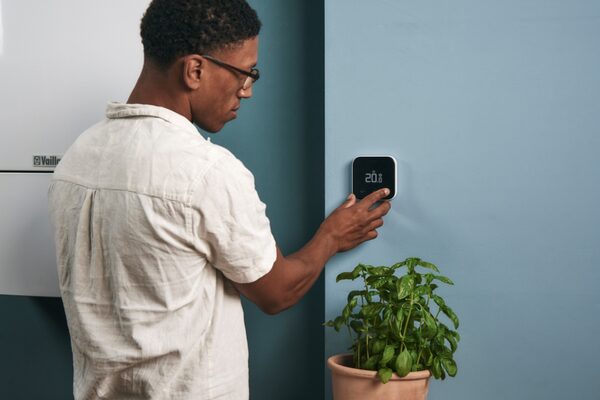 A man adjusting a tado° Smart Thermostat X mounted on a blue wall next to a Vaillant boiler