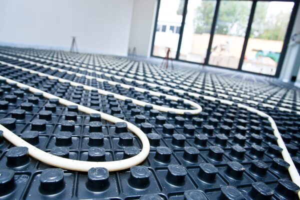 Underfloor heating pipes laid across black studded floor panels in a room under construction