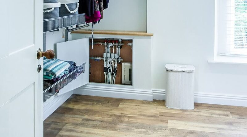 An underfloor heating manifold installed inside a cupboard in a home utility room with wood-effect flooring