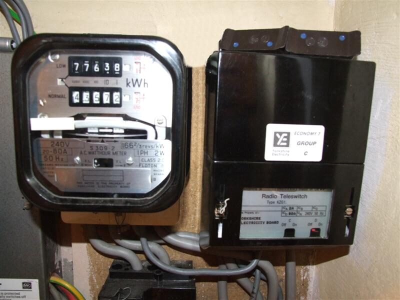 An Economy 7 electricity meter next to a black Radio Teleswitch (Tees 4023) box mounted on a wall with grey cables
