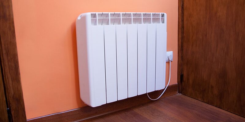 A white electric storage heater mounted on an orange wall next to a wooden door