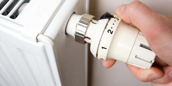 A hand turning the thermostatic radiator valve dial on a white radiator