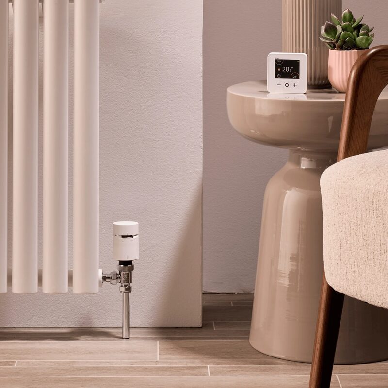 A Wiser smart radiator thermostat valve fitted on a radiator with a Wiser room thermostat on a side table in a styled living room