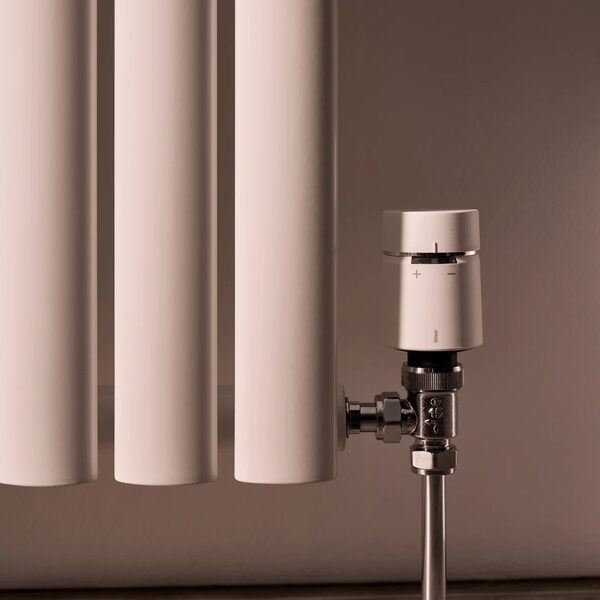 A white Wiser smart radiator thermostat fitted on a valve beside a white column radiator