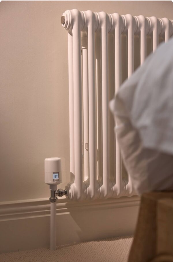 A white Hive smart radiator valve fitted to a column radiator in a bedroom