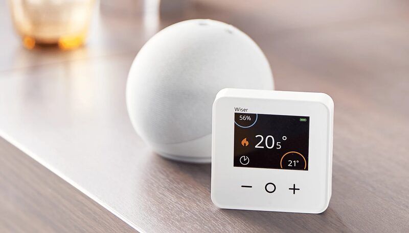 A white Wiser smart thermostat displaying 20.5°C on a wooden table next to a white Amazon Echo smart speaker