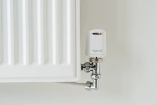 A white Wunda smart thermostatic radiator valve head fitted on the chrome valve of a white panel radiator