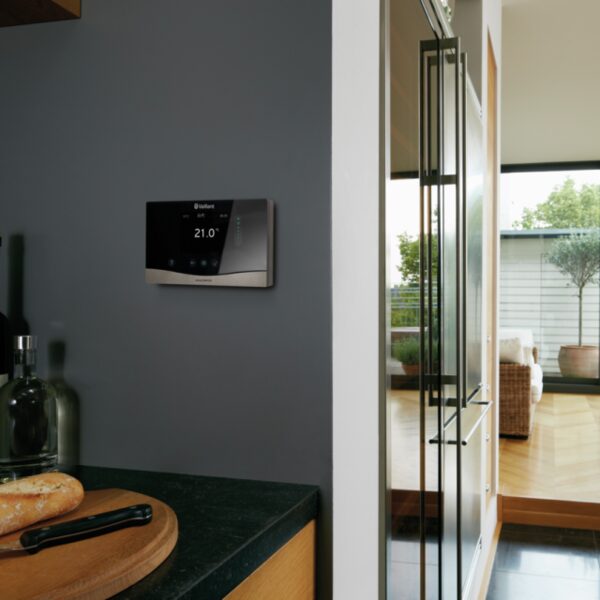 A Vaillant smart room thermostat mounted on a grey kitchen wall, displaying 21.0 degrees