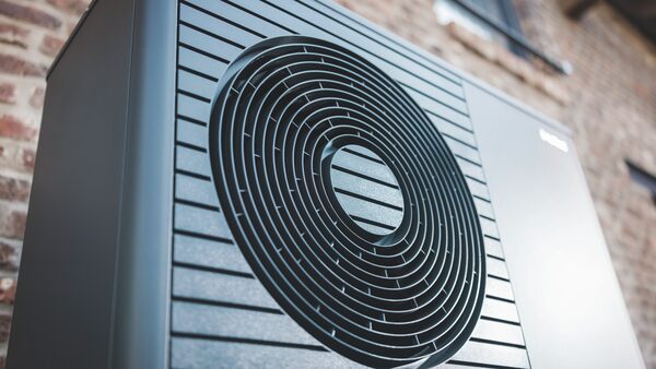 A close-up of a Vaillant aroTHERM plus air source heat pump outdoor unit with its circular fan grille, mounted against a brick wall