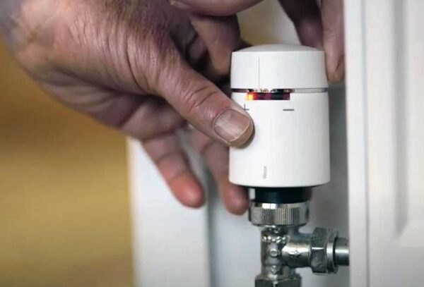A person fitting a white smart thermostatic radiator valve head onto a radiator valve