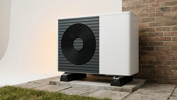 An air source heat pump unit installed outside against a brick house wall on a concrete slab
