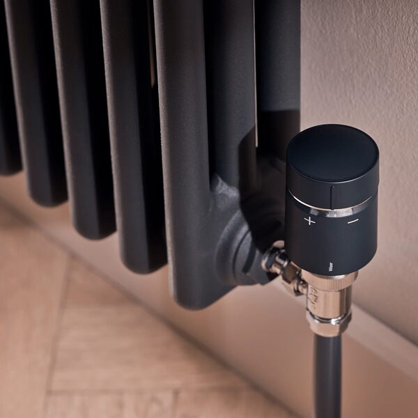 A Wiser smart thermostatic radiator valve (TRV) fitted to a dark column radiator in a home