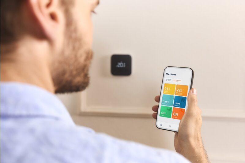 A man controlling a tado° smart thermostat on the wall via the tado° app on his smartphone