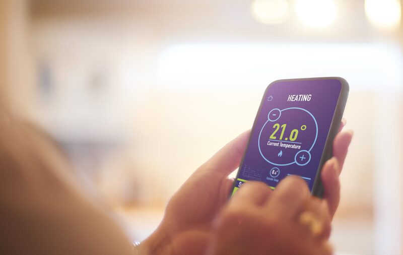 A person holding a smartphone showing a heating control app set to 21.0 degrees