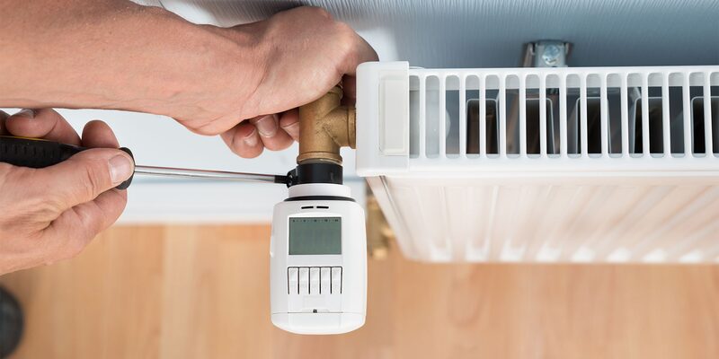 A person using a screwdriver to fit a white smart radiator valve onto a radiator