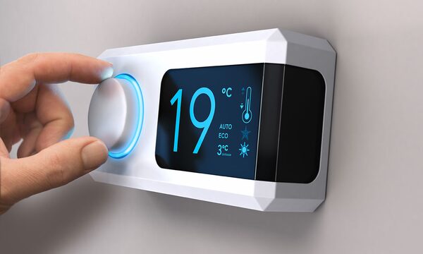 A hand turning the dial on a white digital smart thermostat set to 19°C