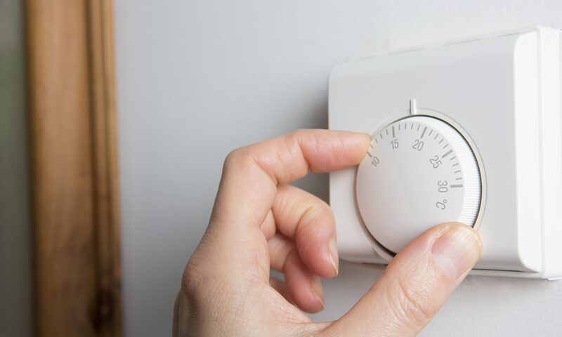 A hand turning the dial on a white wall-mounted room thermostat