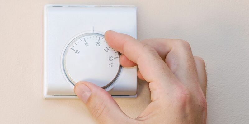 A hand turning the dial of a white wall-mounted room thermostat