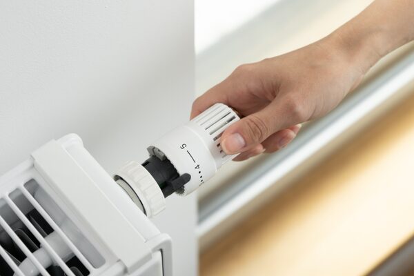 A hand turning the thermostatic radiator valve dial on a white radiator