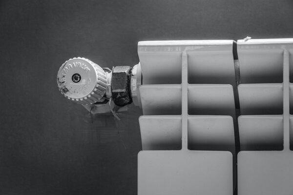 A close-up black-and-white photo of a thermostatic radiator valve fitted to a white panel radiator