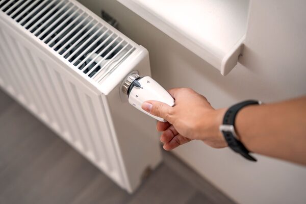 A hand turning the thermostatic valve dial on a white panel radiator in a home
