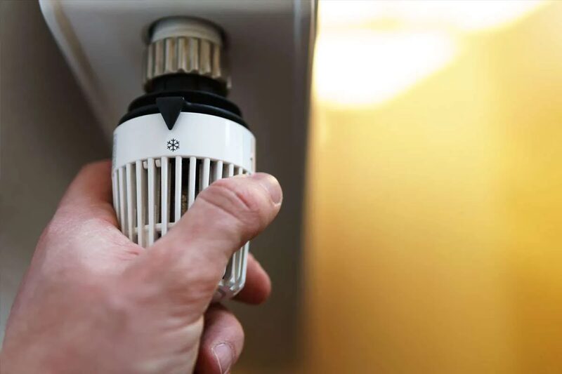 A hand turning a white thermostatic radiator valve (TRV) head on a radiator
