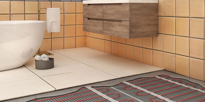 An electric underfloor heating mat with red cables being installed on a bathroom floor next to a freestanding bath and wooden vanity unit