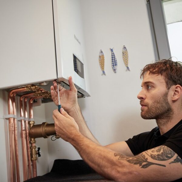 A man using a screwdriver to work on a wall-mounted Vaillant combi boiler with copper pipework underneath