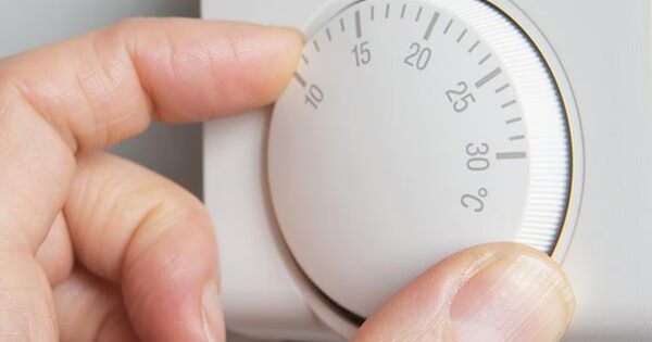 A hand turning a white thermostat dial marked with temperatures from 10 to 30 degrees Celsius