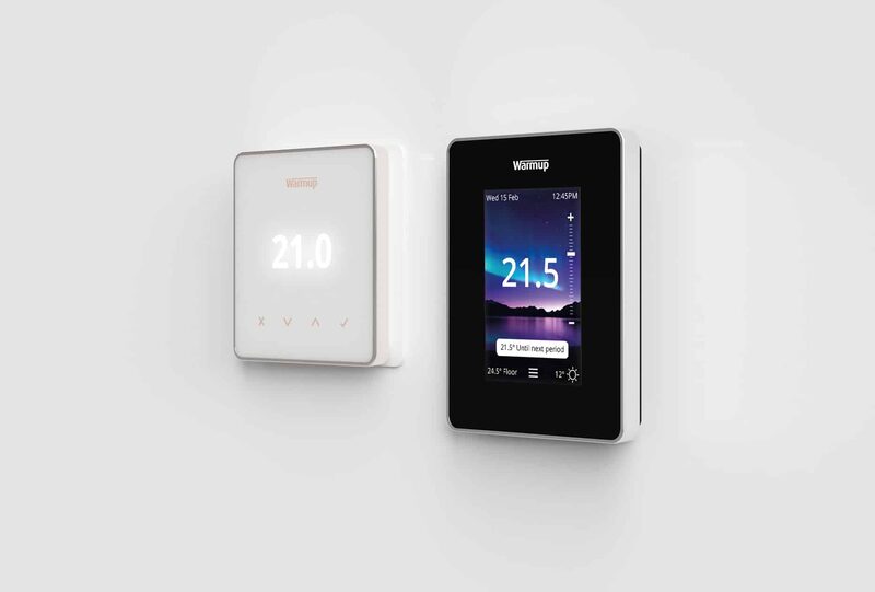 Two Warmup smart underfloor heating thermostats mounted on a white wall, one white and one black touchscreen, both displaying temperatures