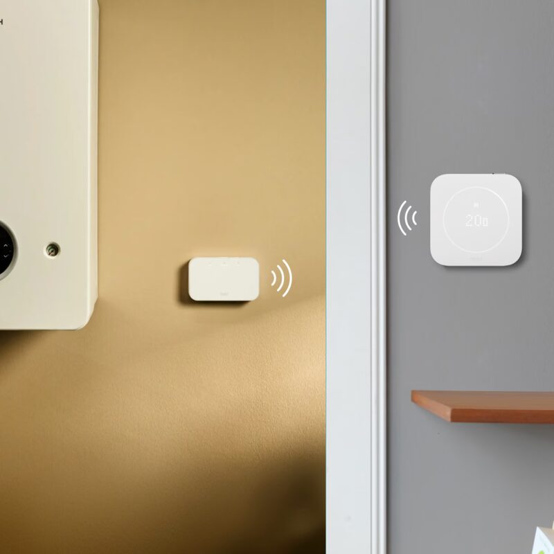 A tado° wireless receiver mounted next to a boiler communicating wirelessly with a tado° smart thermostat showing 20 degrees on a grey wall