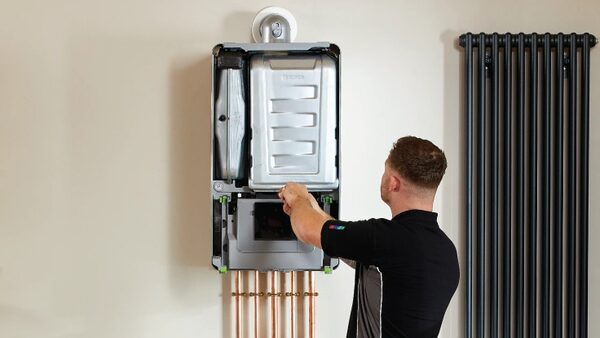 An engineer working on a wall-mounted boiler with its casing removed, next to a black column radiator