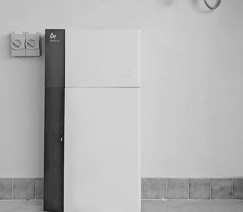 A white and black AlphaESS home battery storage unit standing against a wall next to electrical switches