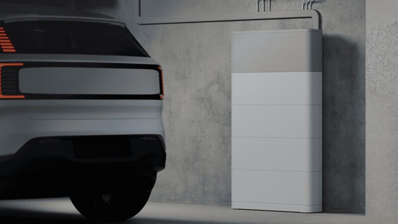 A white home battery storage unit mounted on a concrete garage wall next to a parked electric car