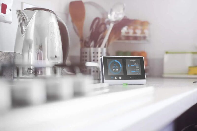 A smart meter display showing energy budget figures on a kitchen counter beside a kettle