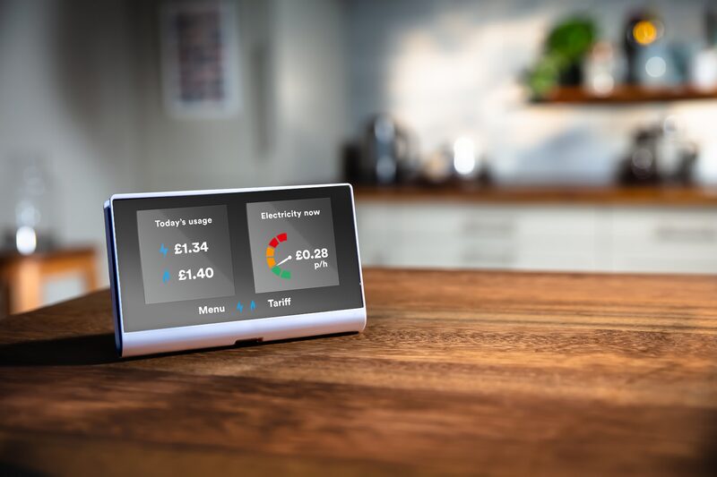 A smart meter in-home display on a wooden table showing today's energy usage and live electricity cost in a kitchen