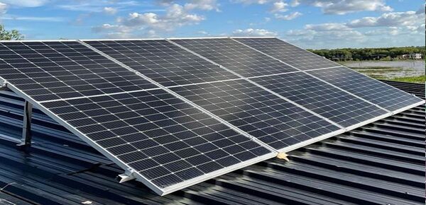 A row of solar panels mounted on a corrugated metal roof under a partly cloudy sky