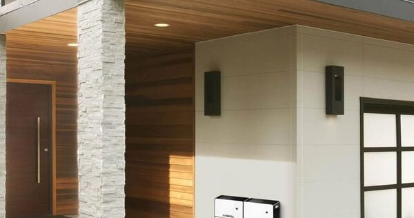 Two white Duracell home battery units mounted on the exterior wall of a modern house next to a garage door