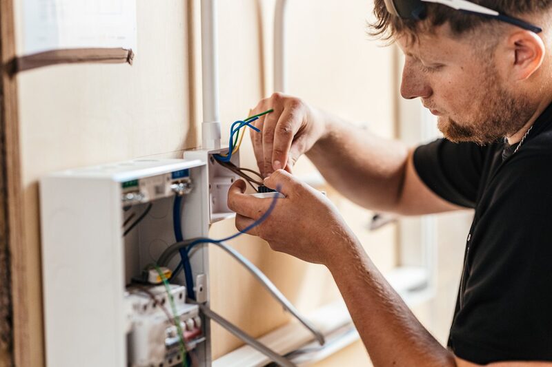 An electrician wiring a domestic consumer unit and electrical connections on a wall